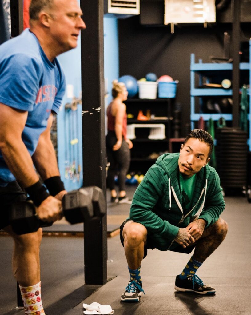 Coach Chris is coaching and helping one of his male clients at the gym.